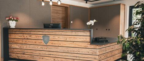 Un mostrador de recepción con detalles de madera, un jarrón con flores y una planta en maceta.