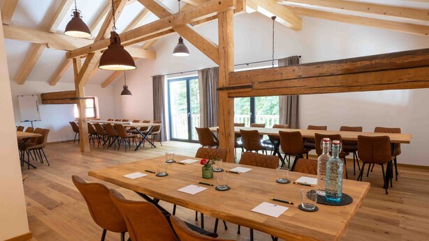 A spacious conference room with wooden tables and chairs, large windows, and exposed wooden beams. - Hotel und Landgasthof Zachschuster (Gaißach)