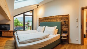 A bedroom with a large bed, a TV, and a view of a green landscape through a large window. - Hotel und Landgasthof Zachschuster (Gaißach)