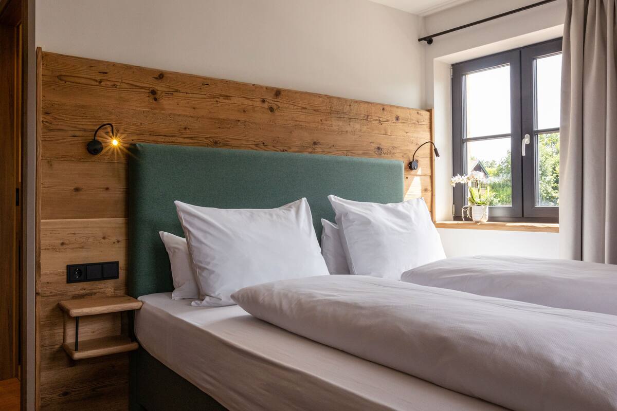A double bed with white linens, a wooden headboard, a bedside table, and a nightstand.