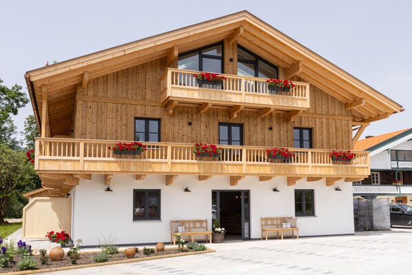 Una cabaña de madera con balcón, puerta principal y un pequeño jardín.