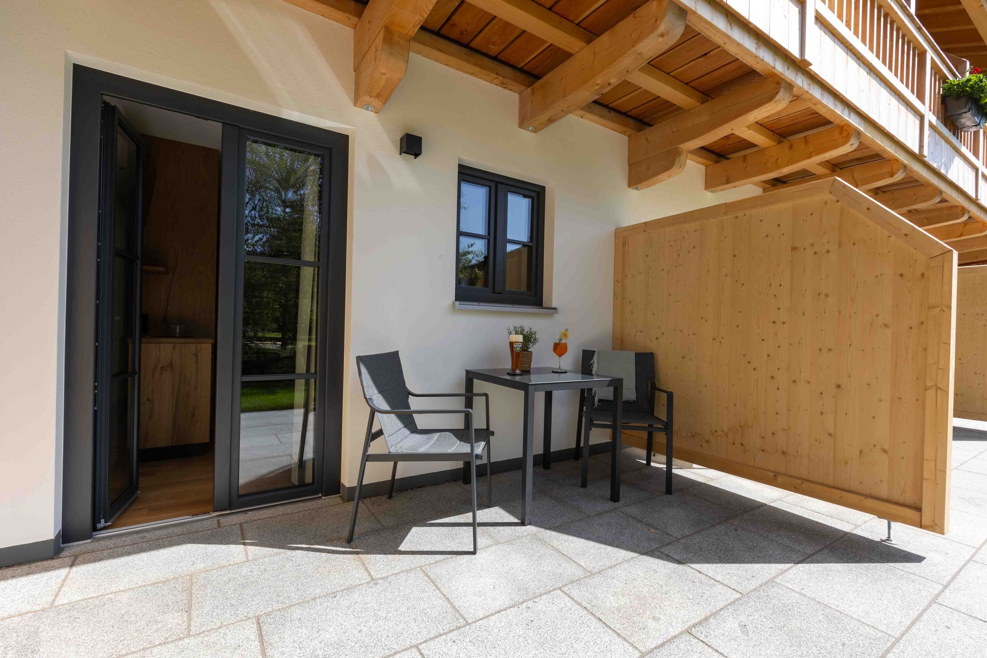 Eine Terrasse im Freien mit Tisch und Stühlen, einem Holzzaun und einem Fenster.