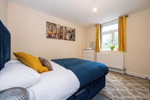 Ein Schlafzimmer mit einem Bett, einem Heizkörper, einem Fenster mit gelben Vorhängen und einem Bild an der Wand.