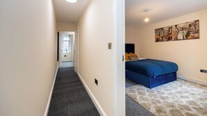 A hallway leading to a bedroom with a bed, a painting, and a door. - Stunning 3 Bedroom Home in Newcastle-under-lyme With Garden (Newcastle-Under-Lyme)