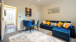 A modern living room with a blue sofa, two blue chairs, a white fluffy rug, and a painting on the wall. - Stunning 3 Bedroom Home in Newcastle-under-lyme With Garden (Newcastle-Under-Lyme)
