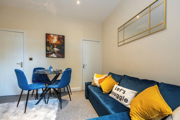 A room with a blue sofa, two blue chairs, a small table, and a painting on the wall. - Stunning 3 Bedroom Home in Newcastle-under-lyme With Garden (Newcastle-Under-Lyme)