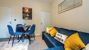 A room with a blue sofa, two blue chairs, a small table, and a painting on the wall. - Cosy 4 Bed Townhouse Near Keele University and Royal Stoke Hospital (Newcastle-Under-Lyme)