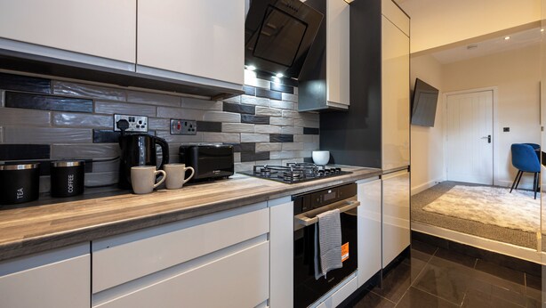 A modern kitchen with white cabinets, a built-in oven, and a coffee maker. - Cosy 4 Bed Townhouse Near Keele University and Royal Stoke Hospital (Newcastle-Under-Lyme)