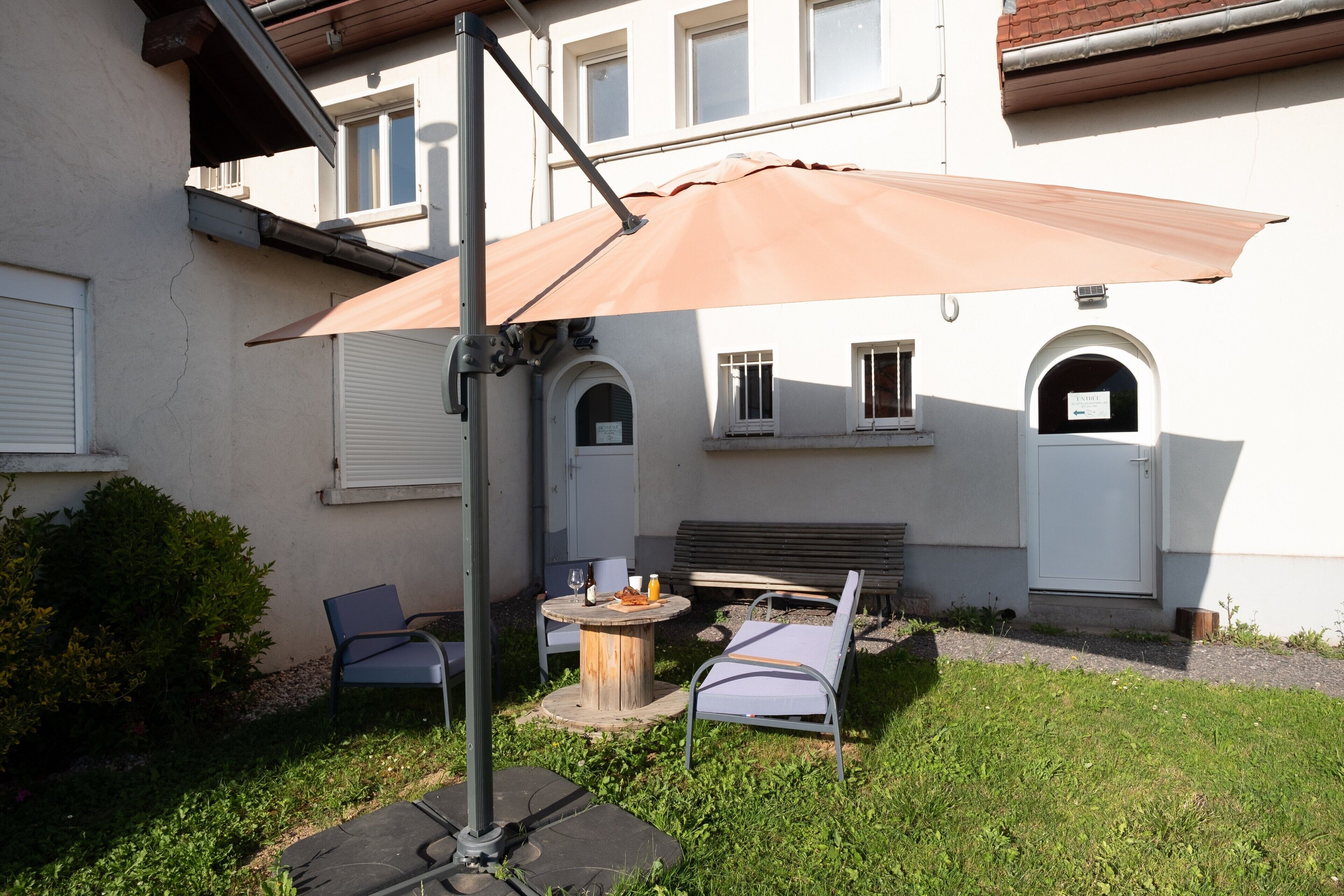 Ein Außenbereich mit Sitzgelegenheit, Tisch, Stühlen und einem großen Sonnenschirm.