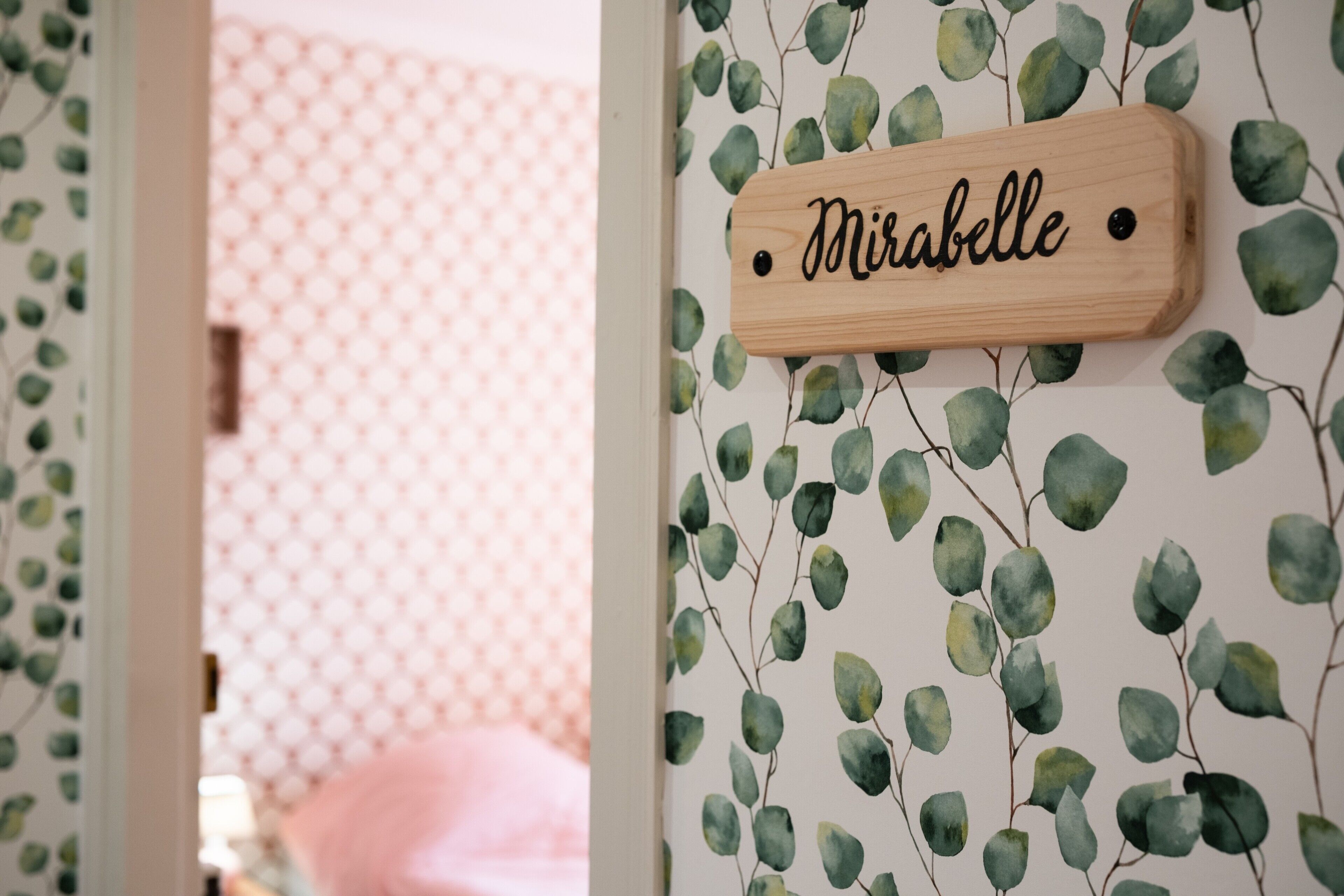 A wooden sign with the name 'Mirabelle' on a wall with a leafy pattern.