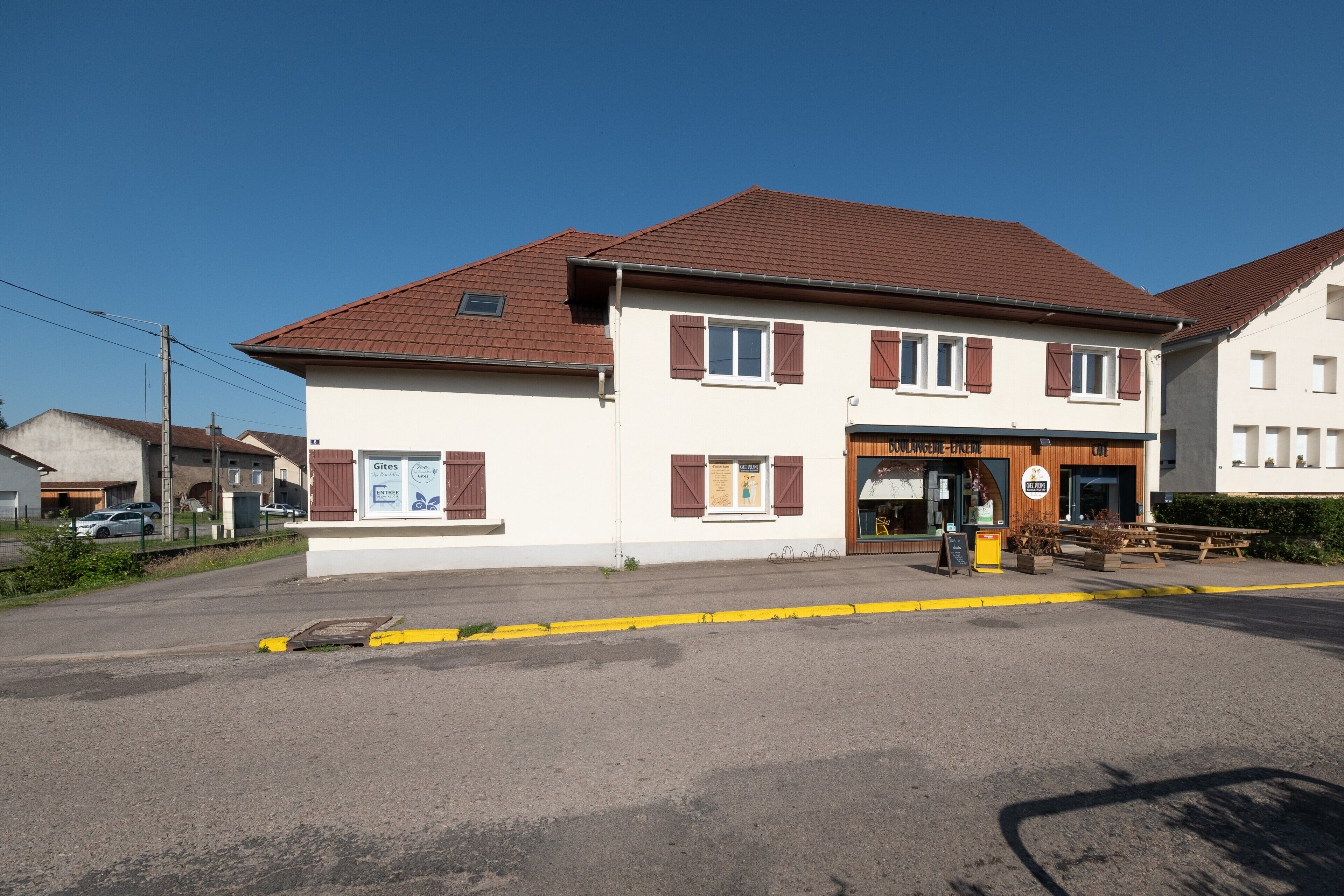 A two-story building with a brown roof and white walls, featuring a storefront with a sign that reads 'Gites.'