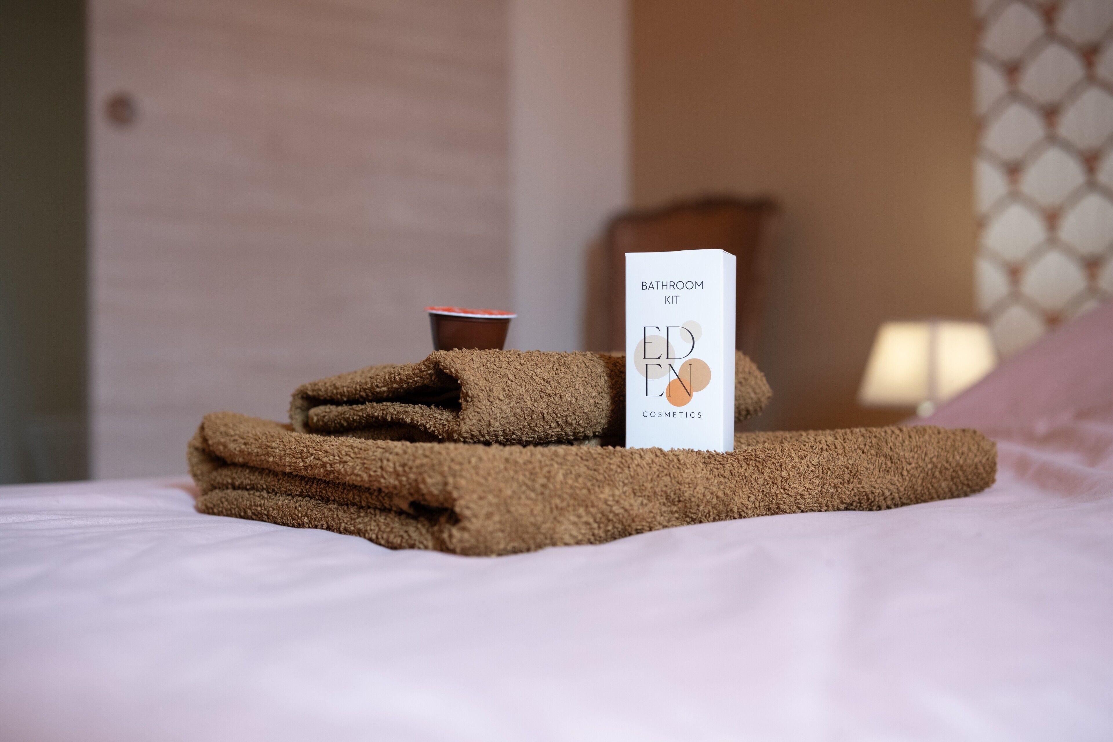 A neatly made bed with a towel, a cup, and a bathroom kit on it.