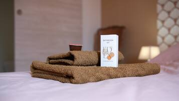 A neatly made bed with a towel, a cup, and a bathroom kit on it.