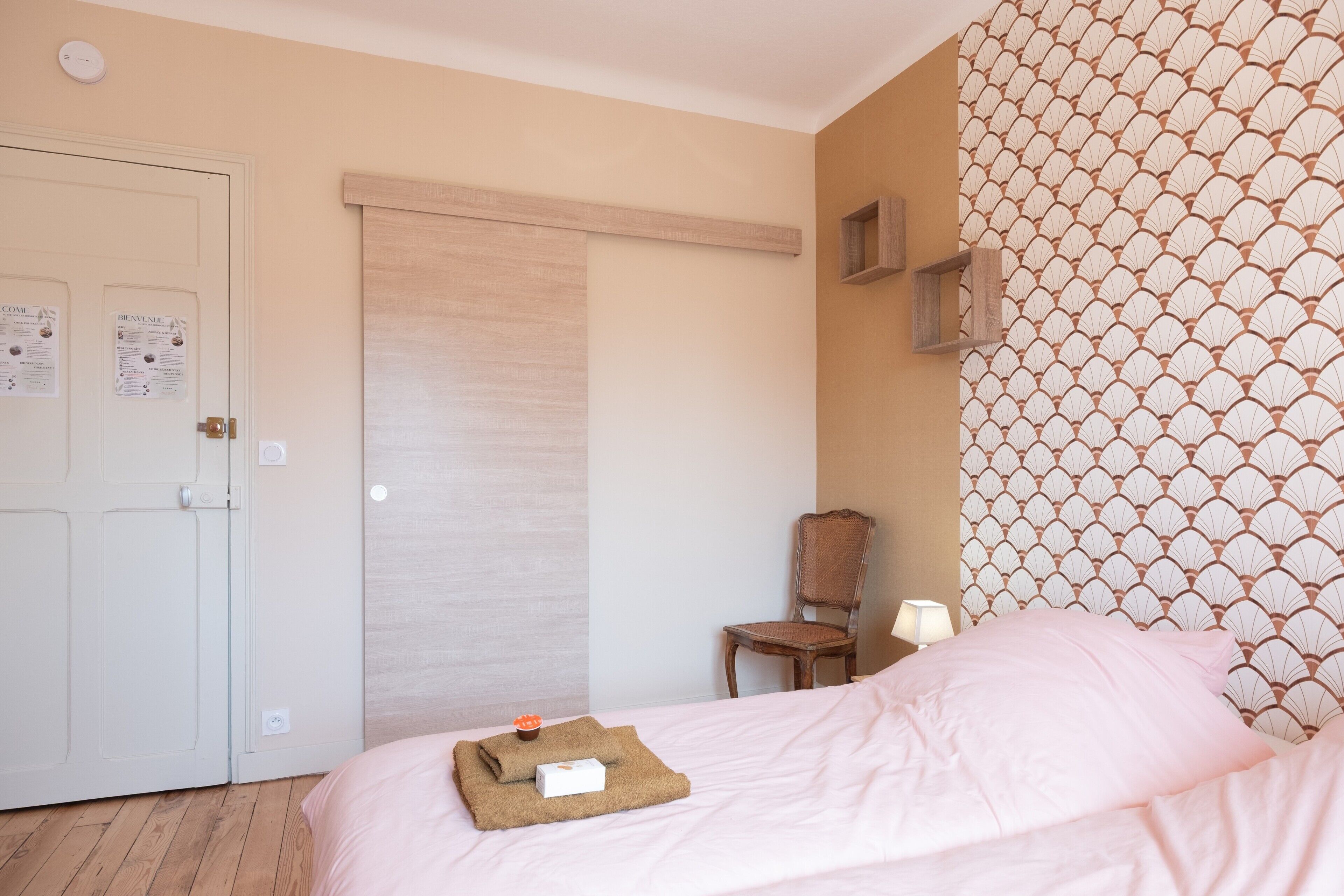 A hotel room with a bed, a chair, a wardrobe, and a patterned wall.
