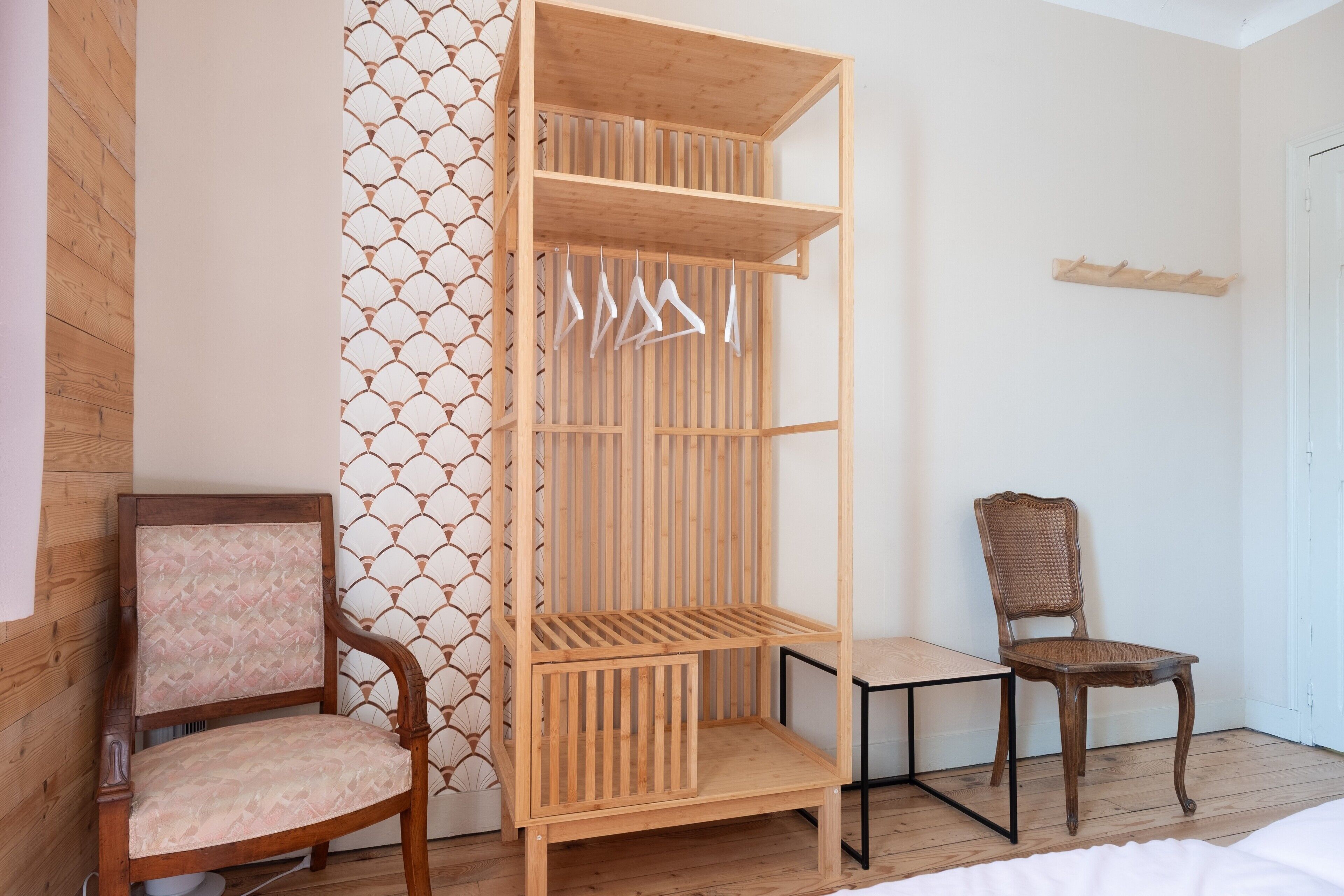 Une pièce dotée d’un plancher en bois, d’une chaise en bois avec un siège rembourré, d’une armoire en bois avec une tringle pour suspendre les vêtements, et d’un mur orné d’un motif géométrique.