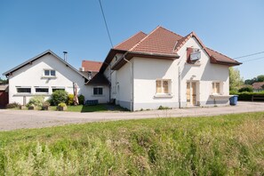A two-story house with a sloped roof, a garage, and a front yard. - Jonquille Room with Wi-Fi (Brû)