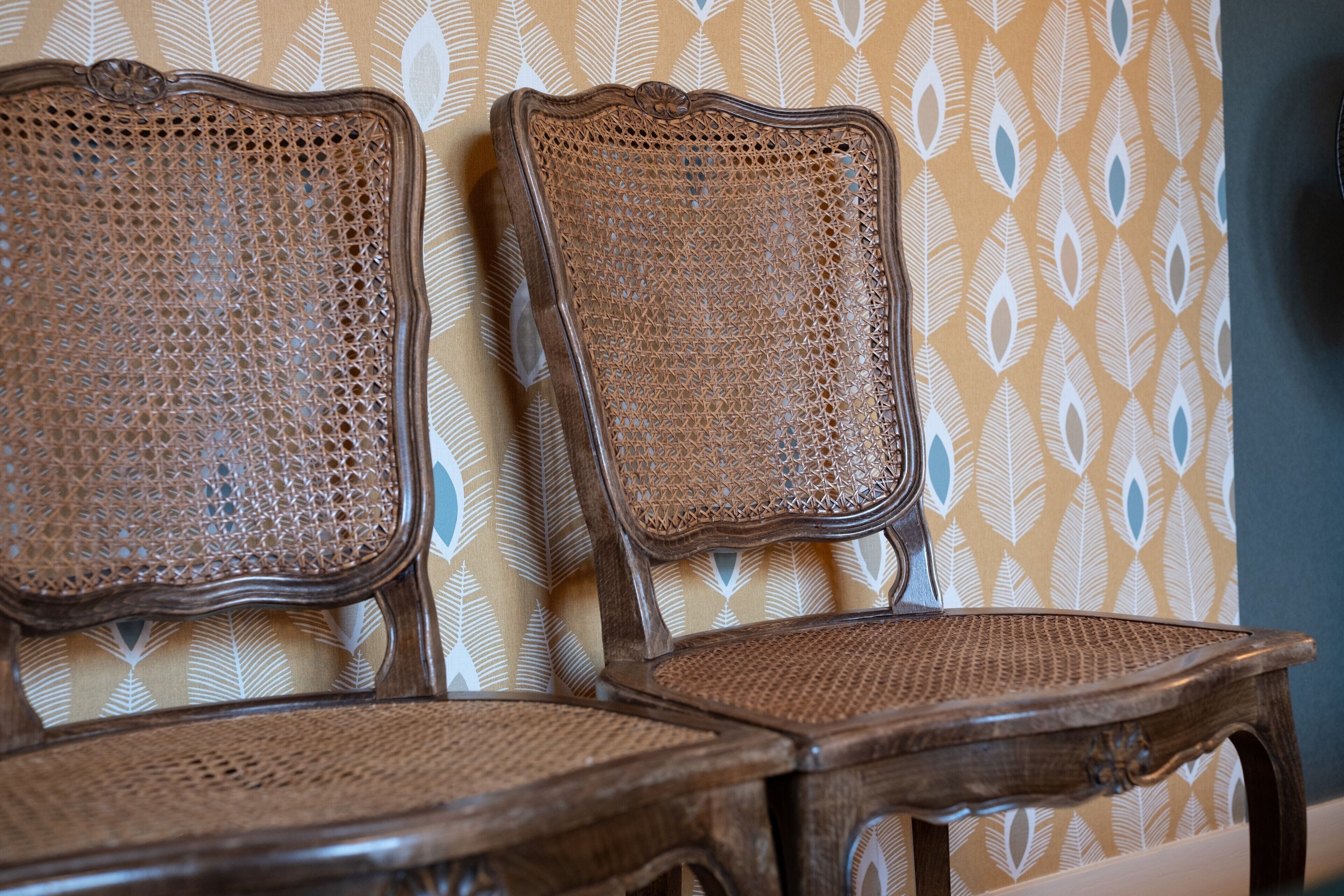 Two wooden chairs with woven seats and backs against a patterned wall.