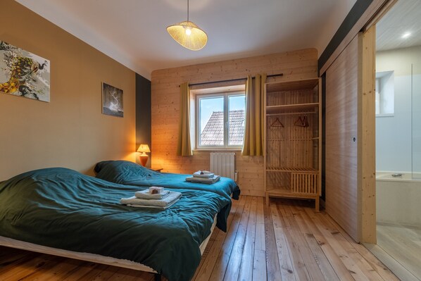 A room with two beds, a window with curtains, a radiator, and a wooden wardrobe. - Jonquille Room with Wi-Fi (Brû)