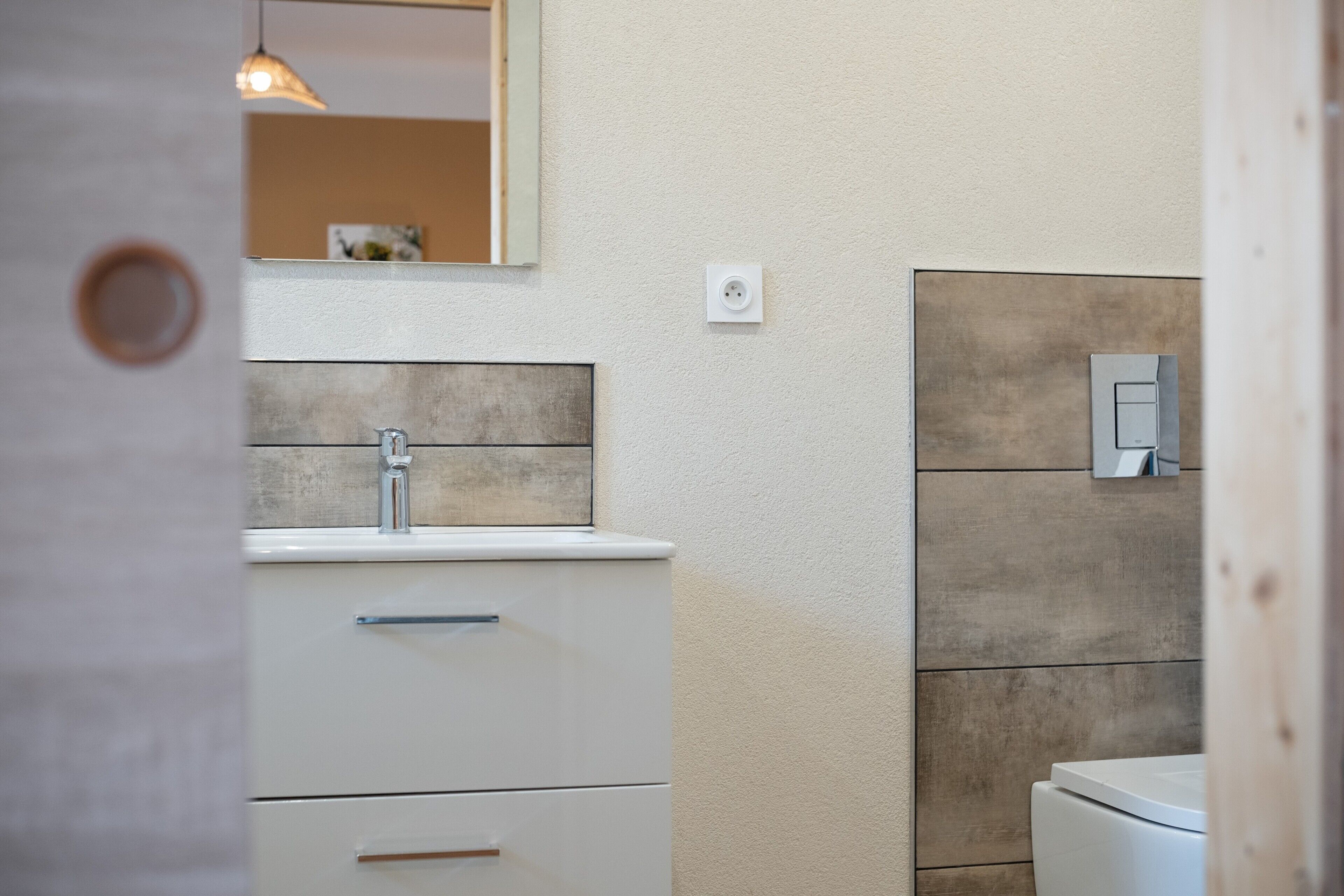 Une salle de bain avec un lavabo blanc, un miroir et un panneau mural en bois.