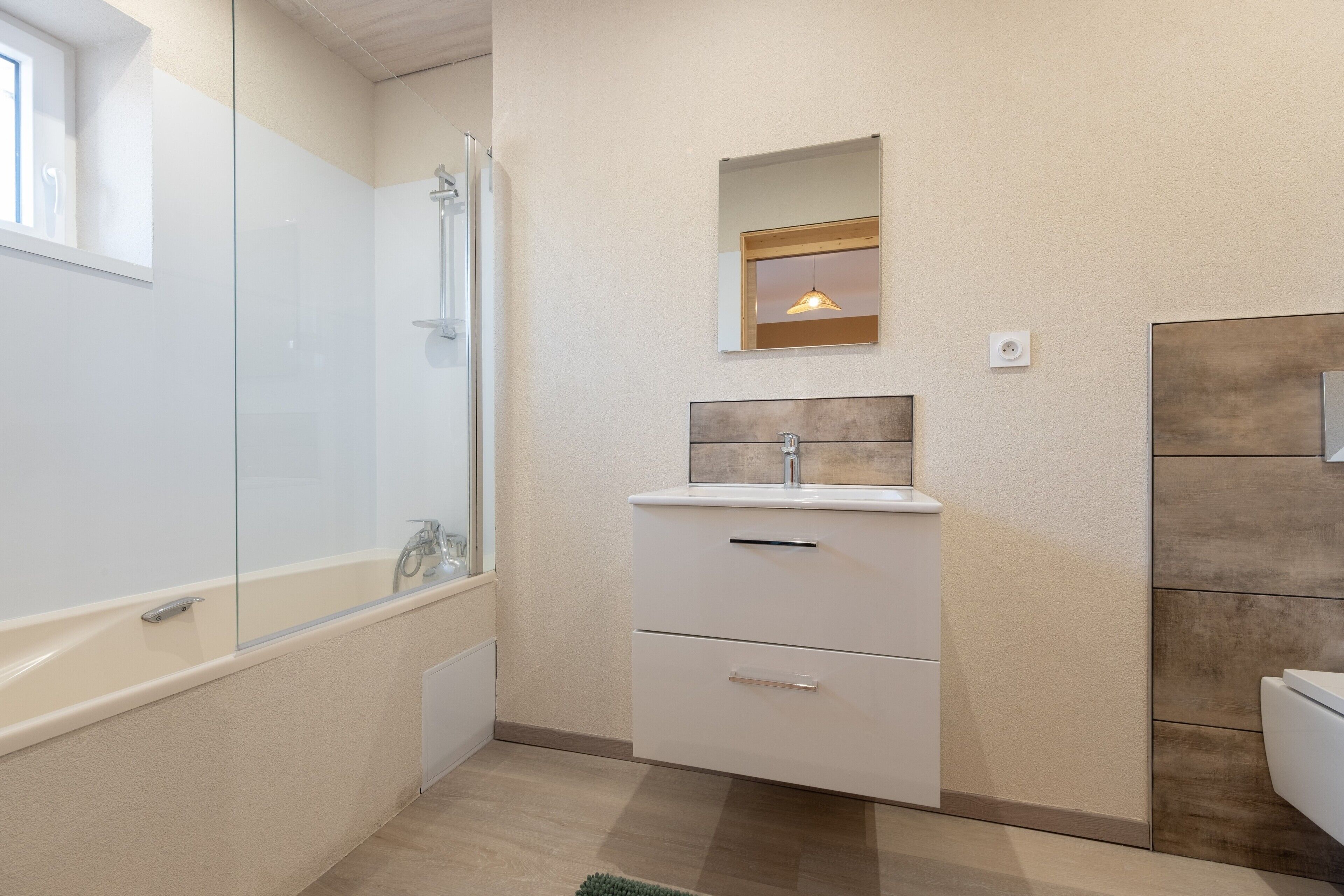 A bathroom with a glass-enclosed shower, a white vanity with a mirror, and a wooden accent wall.