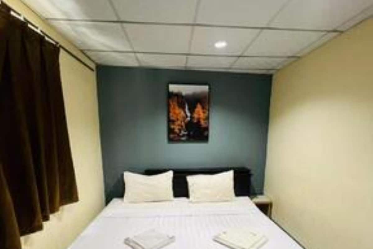 Habitación de hotel con una cama grande, una mesita de noche, un cuadro colgado en la pared y una ventana con cortinas.