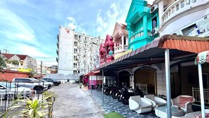 Vista de la calle con una hilera de edificios coloridos, un espacio exterior cubierto con sofás y motocicletas estacionadas.