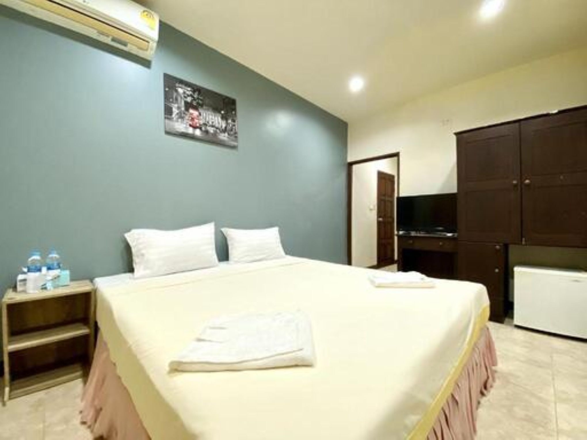 Habitación de hotel con cama, mesita de noche con botellas de agua, televisor y armario.