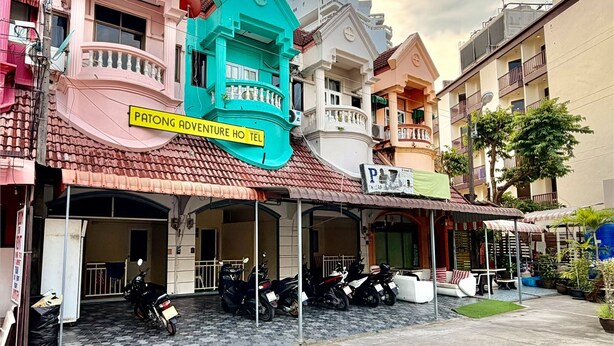 Un hotel con fachada colorida, un letrero que dice 'Patong Adventure Hotel' y varias motocicletas estacionadas adelante.