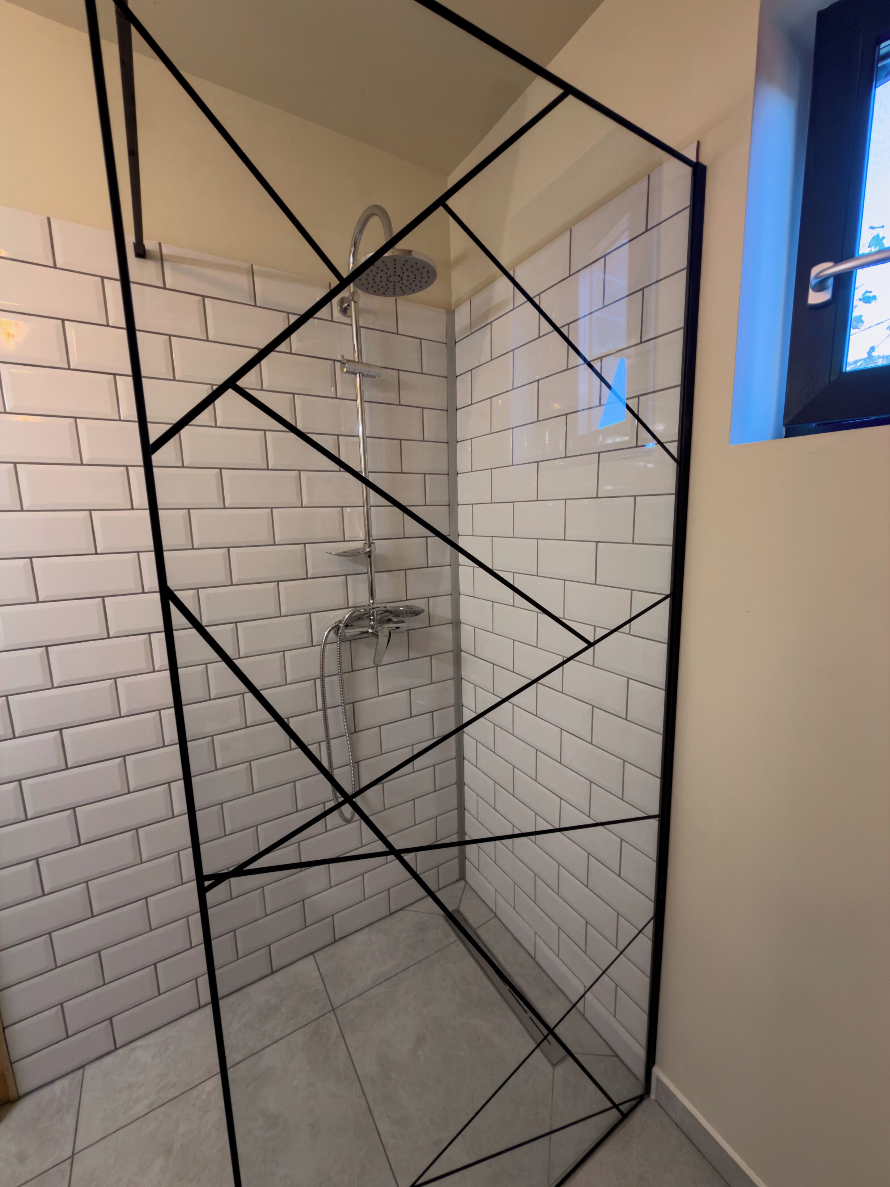 Douchecabine met witte betegelde wanden en een zwart metalen frame.