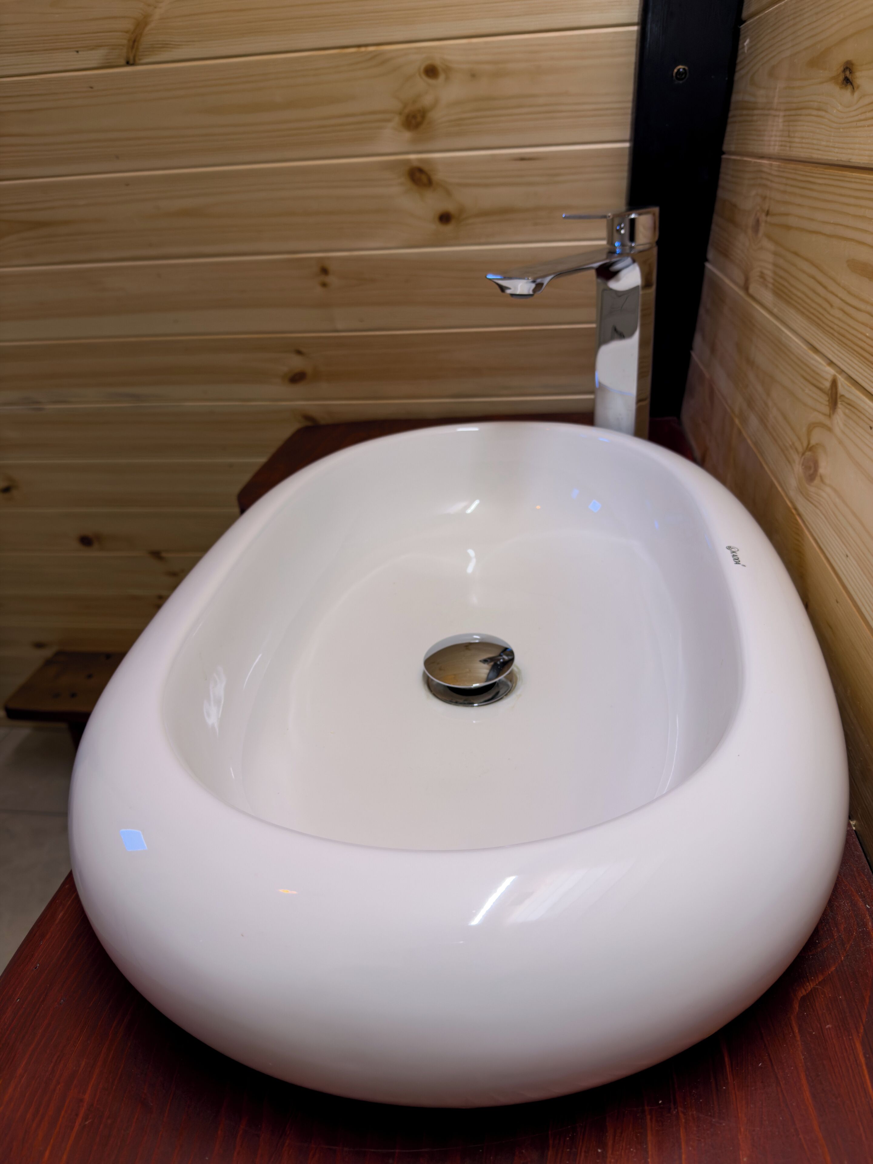 Un lavamanos blanco ovalado con desagüe, paneles de madera en las paredes y una encimera de madera.