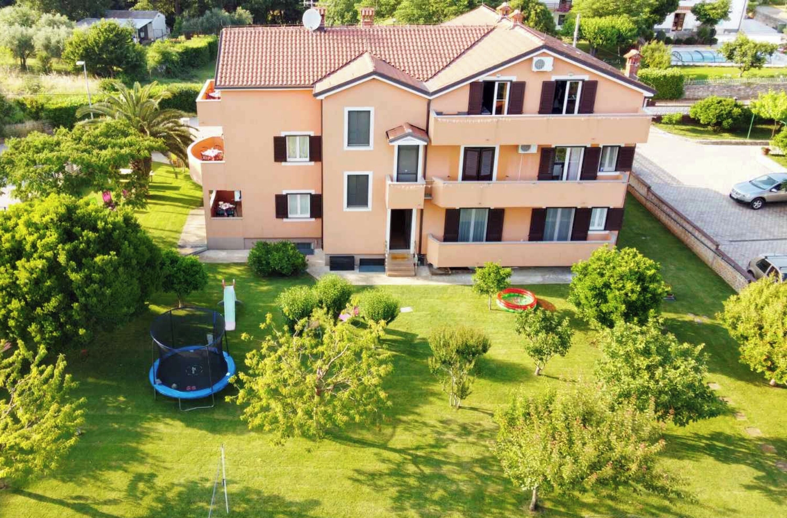 Un edifici residencial de diversos pisos amb balcons, un jardí ben cuidat i un trampolí.