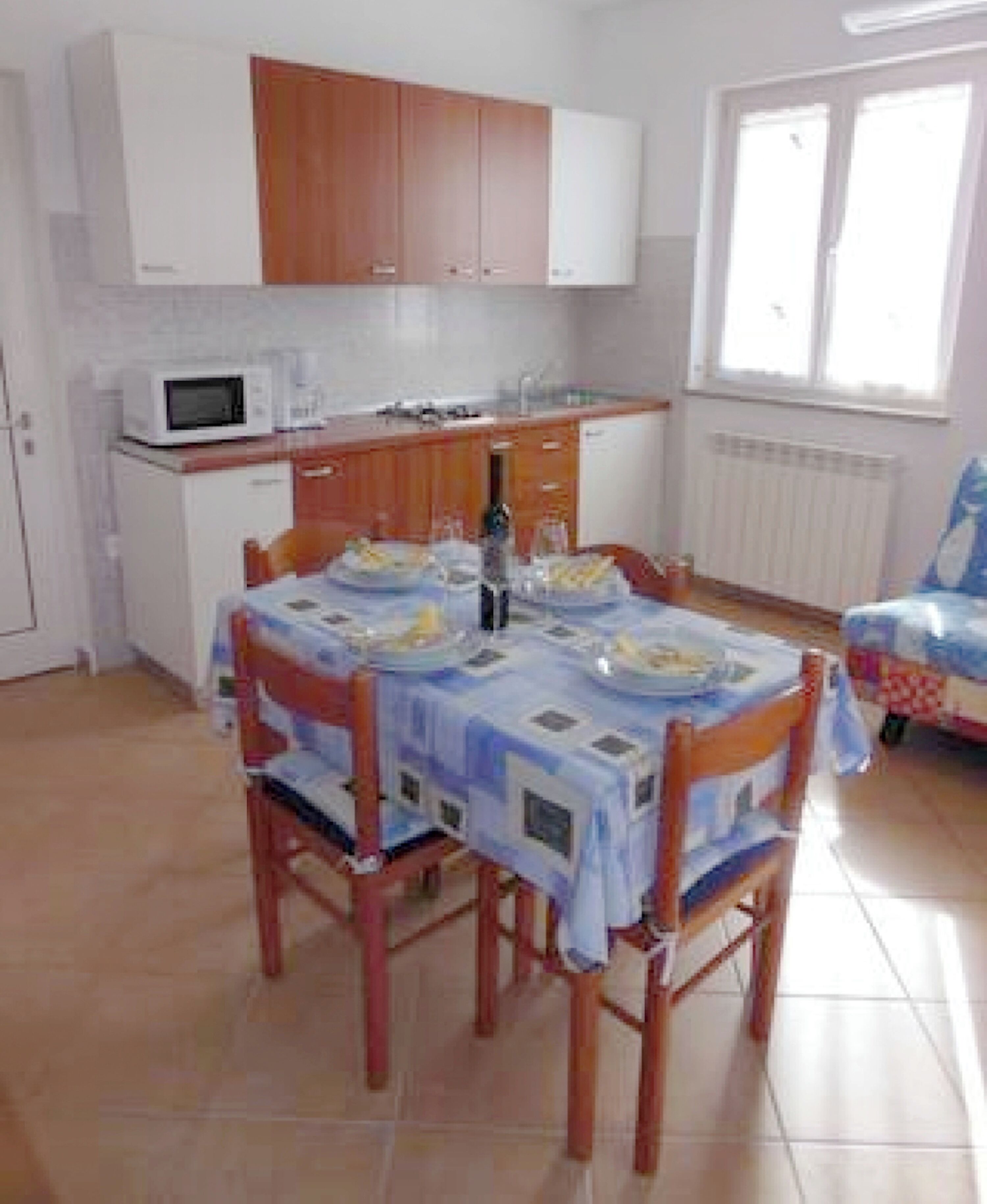 Cuina compacta amb armaris blancs, microones i zona de menjador amb taula preparada per a dues persones.