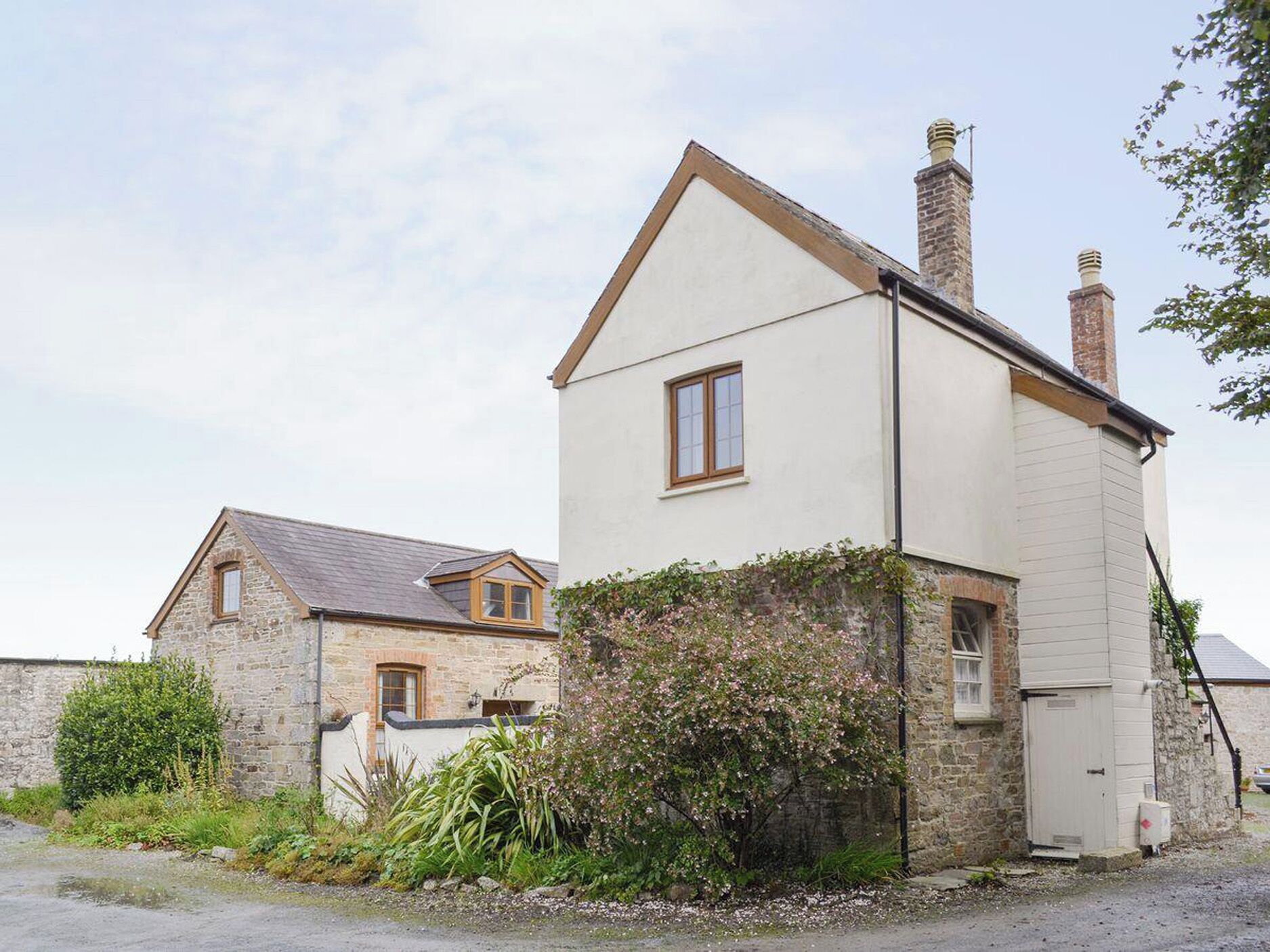 Une maison à deux étages avec une façade en pierre, une cheminée et un petit jardin agrémenté de plantes à fleurs.