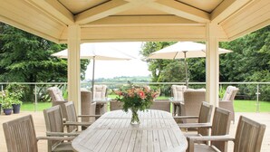 Une terrasse extérieure couverte, avec une table ronde et des chaises en osier, entourée de plantes en pot et de parasols.