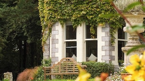 Un bâtiment en pierre recouvert de lierre, un banc et un jardin fleuri.