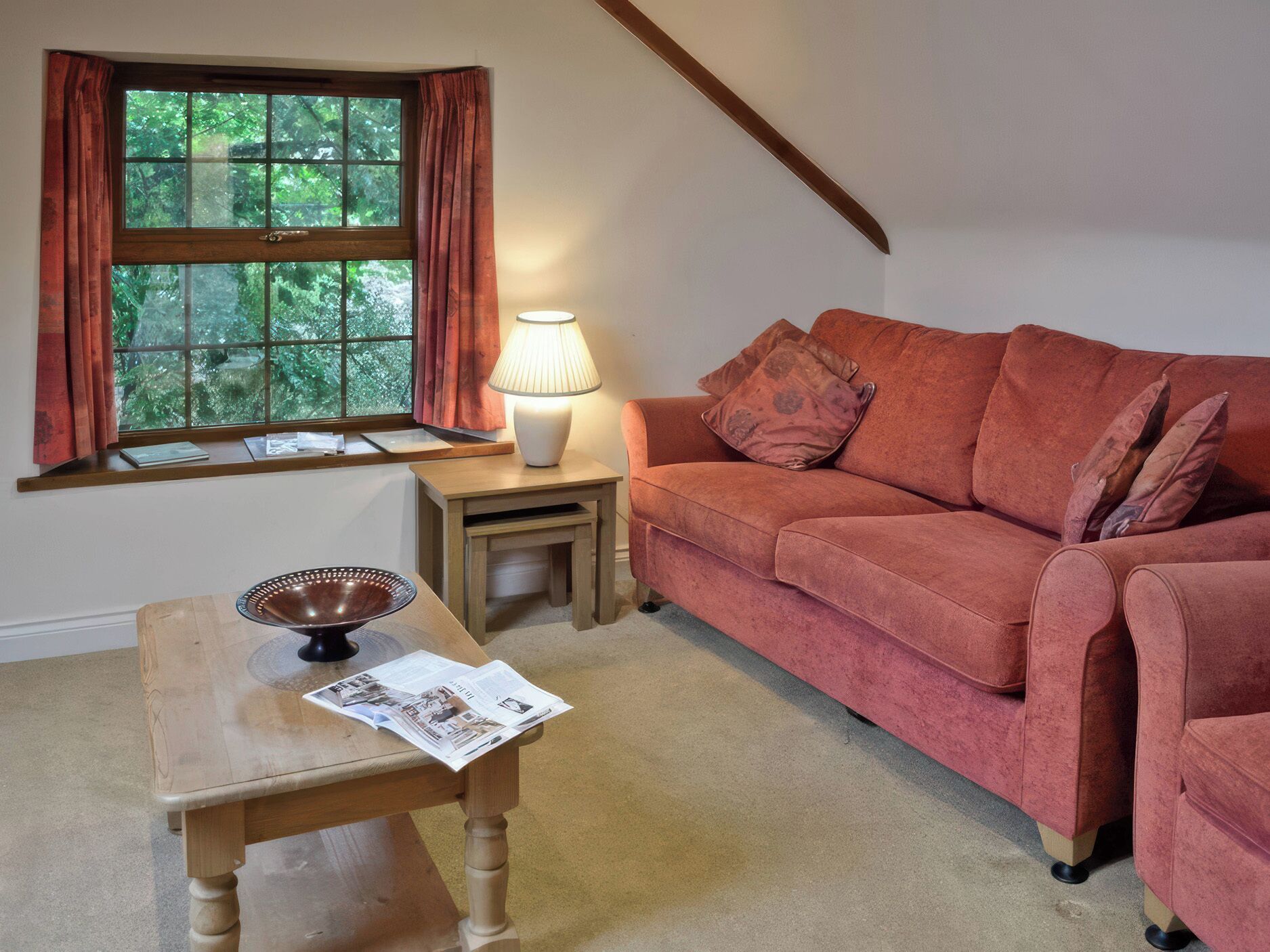 Una sala de estar acogedora con una mesa de madera, un sofá rojo, una ventana con cortinas y una lámpara.