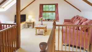 Une pièce de style « loft » avec un plafond en pente, une télévision, une table avec un vase, un canapé et une fenêtre avec des rideaux.