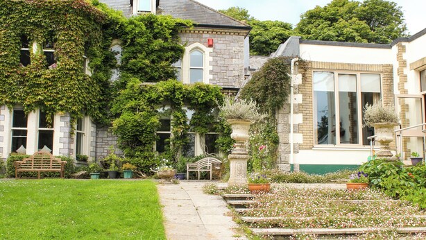 Un bâtiment traditionnel en pierre, dont les murs sont recouverts de lierre, avec un chemin en pierre et un jardin fleuri.