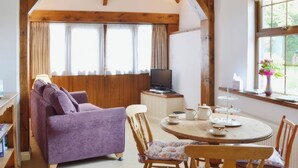 A cozy room with a purple sofa, wooden chairs, a round table with a teapot, and a TV on a wooden cabinet. - Farrier Cottage (Falmouth)