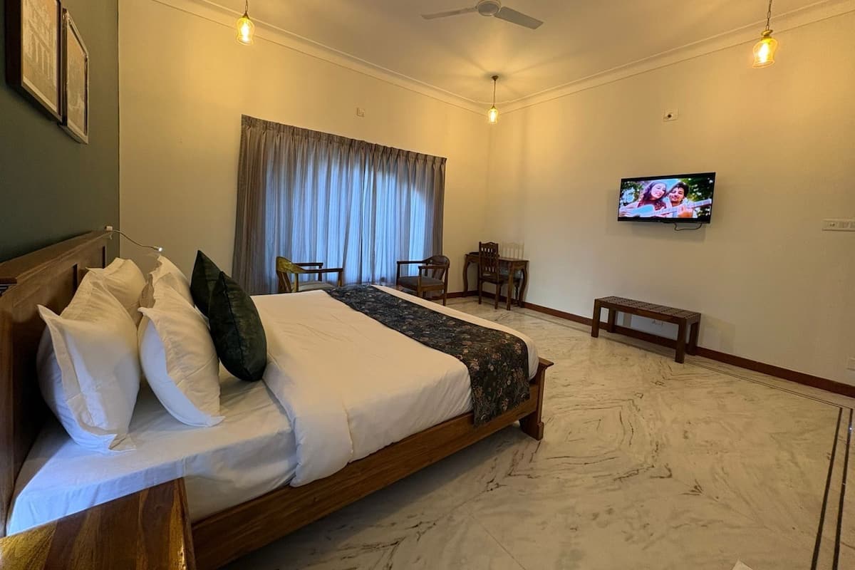 A hotel room with a large bed, a TV on the wall, a ceiling fan, and a window with curtains.