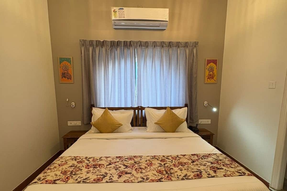 A bedroom with a wooden bed, two bedside lamps, an air conditioning unit, and a window with curtains.