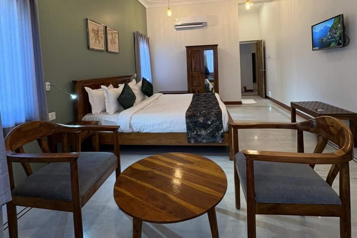 A hotel room with a bed, wooden chairs, a round wooden table, a ceiling fan, and a TV on the wall.