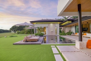 Ein modernes Haus mit Pool, Sitzgelegenheit im Freien und einem gepflegten Rasen.
