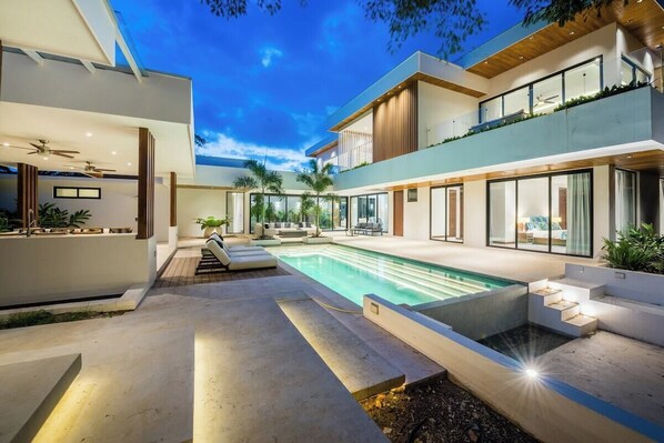 Una casa moderna con piscina, mobiliario exterior y un ventanal grande con vistas a la piscina.