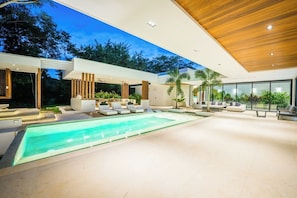 Ein moderner Poolbereich im Freien mit Liegestühlen und einem gläsernen Wohnraum.
