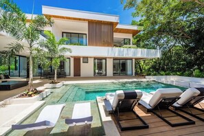 Una casa moderna de dos pisos con piscina, mobiliario exterior y abundante vegetación.