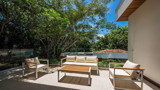Un espacio al aire libre con sofás, dos sillones, una mesa de madera y una pared de cristal.