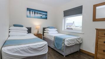 Un dormitorio con dos camas individuales, una mesita de noche con lámpara, un ventanal con vistas y un aparador de madera.
