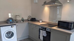 A compact kitchen with a washing machine, a microwave, a toaster, and a kettle. - Horseshoe Cottage (Falmouth)