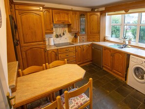 A kitchen with wooden cabinets, a dishwasher, a sink, and a window with a view of greenery. - Dunns Cottage (Swansea)